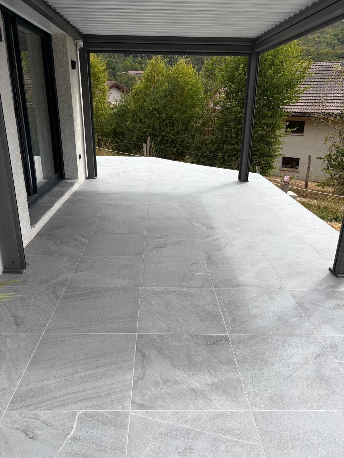 Terrasse en carrelage grand format gris sous pergola, vue sur la vallée du Haut-Jura